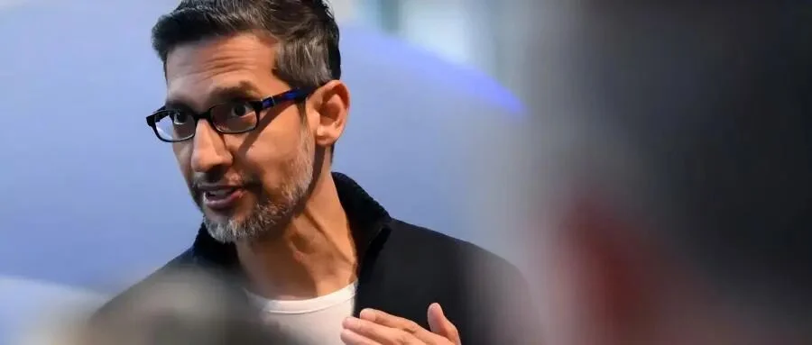 Google CEO Sundar Pichai speaking and gesturing, with blurred audience members in the foreground.